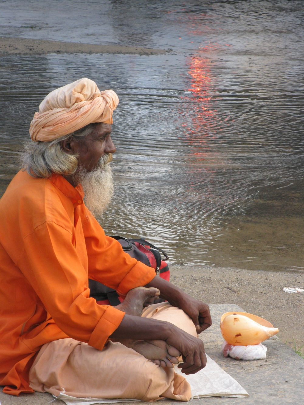 Mann in oranger Kleidung sitzt am Ufer eines Flusses in Indien