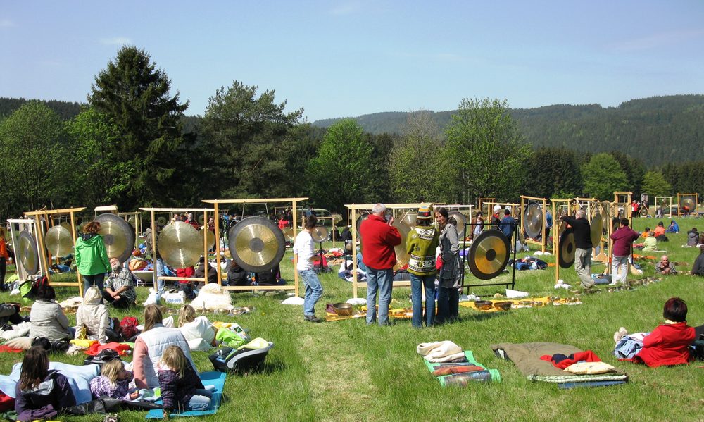 Menschen sitzen und liegen auf einer Wiese vor aufgebauten Gongs