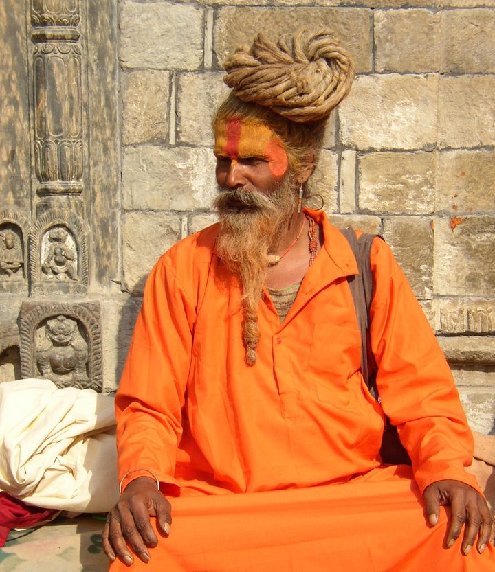 Sadhu in oranger Kleidung sitzt an einer Steinmauer