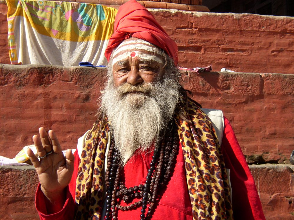 Sadhu mit rotem Turban und weißem Bart vor einer Ziegelmauer