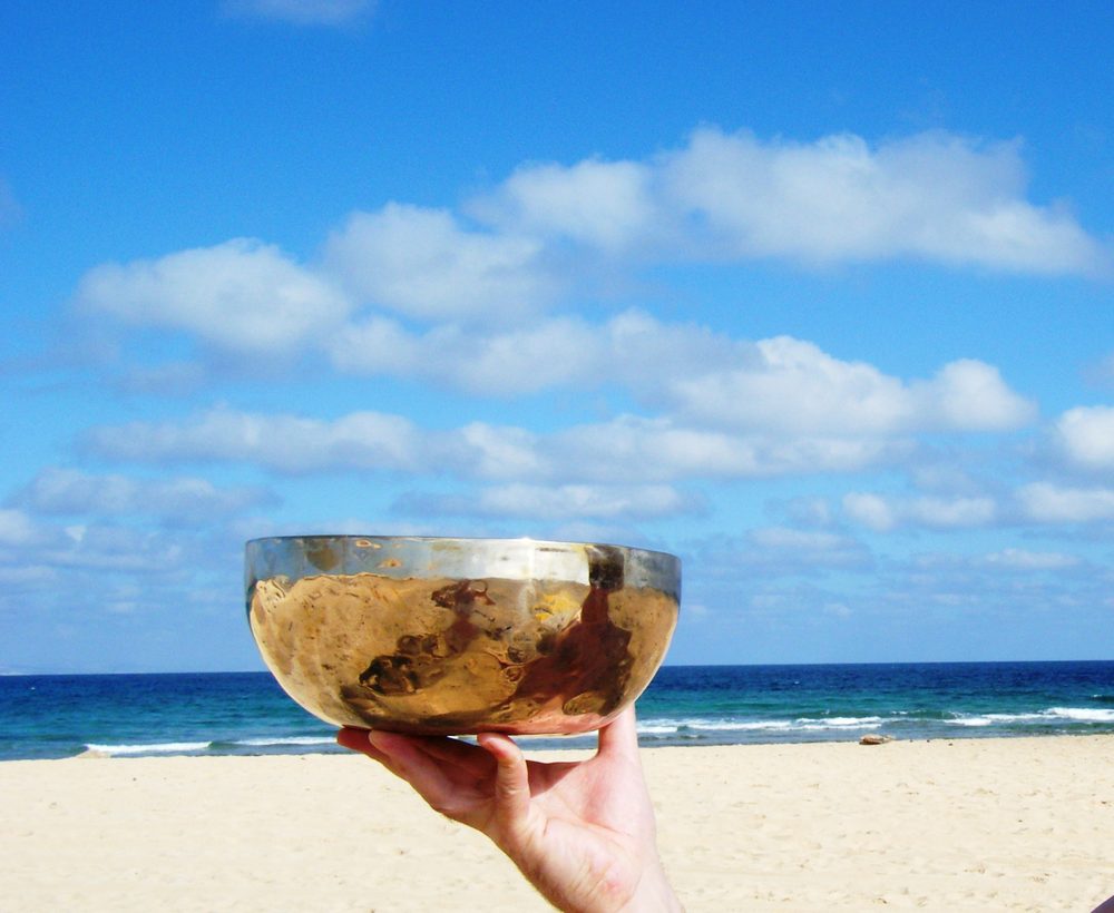 Klangschale wird am Strand in der Hand gehalten