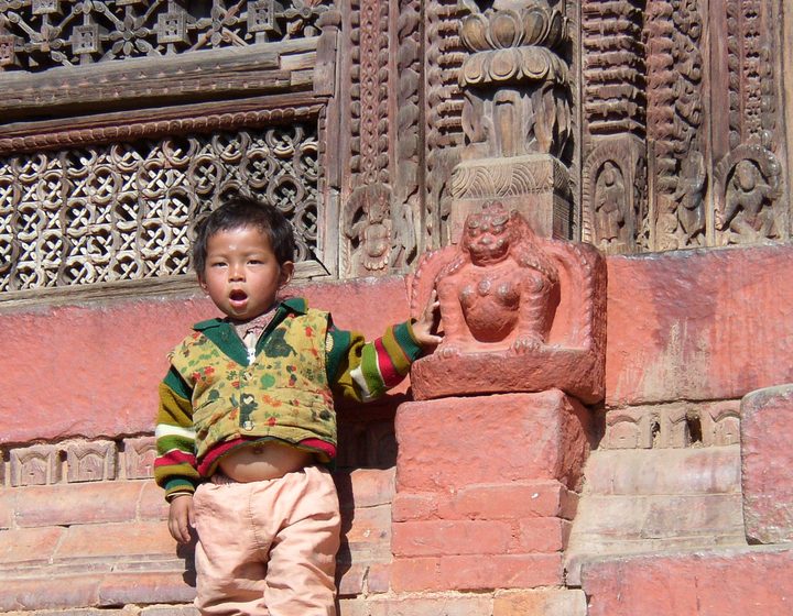 Kind vor einer reich geschnitzten Tempelfassade in Nepal